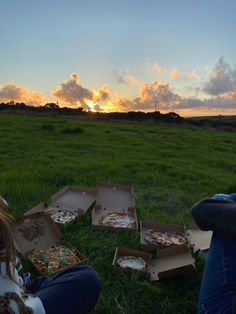 people sitting in the grass eating pizza at sunset