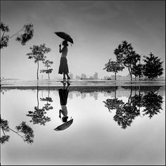 a black and white photo of a woman holding an umbrella over her head while standing in the water