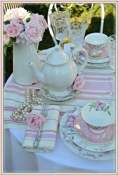 a pink and white table setting with teapot, plates, napkins and flowers