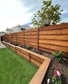 a long wooden fence with flowers in the middle and green grass on both sides next to it