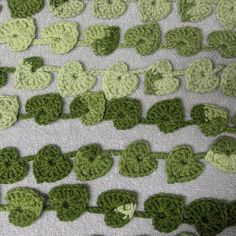 crocheted green leaves are arranged in rows on a white surface with gray background