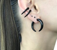 a woman's ear is adorned with black acrylic hoops and two small spikes