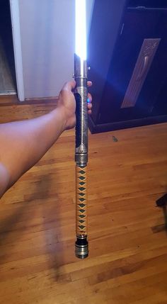 a person holding a light saber in their hand on top of a hard wood floor