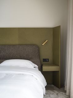 a bed with white sheets and pillows in a bedroom next to a wall mounted lamp