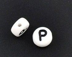 two white and black plastic buttons with the letter p on each one, sitting on a black surface