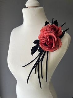 a white mannequin with a red rose on it's head and black feathers