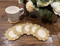 four crocheted coasters on a table next to a coffee cup and flowers