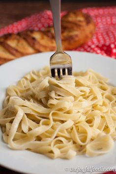 a fork is stuck into some pasta on a plate with bread in the back ground