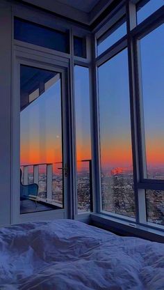 a bedroom with large windows and a view of the city at sunset or dawn from it