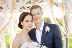 a bride and groom pose for a photo under an arch decorated with ribbons at their wedding