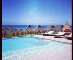 an empty swimming pool with chaise lounges next to the water and beach in the background