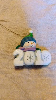 a snowman ornament hanging from a string on a bed with white sheets