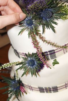 a person is placing flowers on top of a wedding cake with purple and green decorations