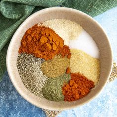 a bowl filled with different colored spices on top of a blue cloth next to a green napkin