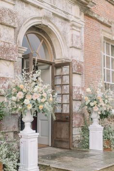 three white vases filled with flowers on top of a stone step next to a building