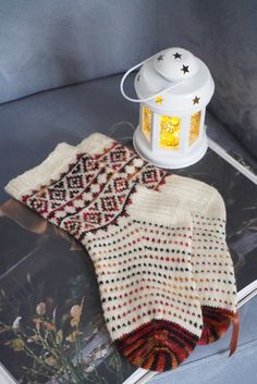 a knitted mitt next to a lantern on top of a magazine