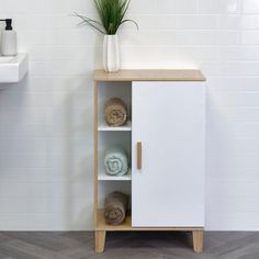 a white cabinet with towels and a plant in it next to a toilet paper dispenser