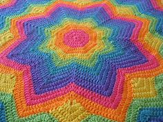 a multicolored crocheted blanket is laying on the floor with it's center