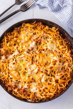 a skillet filled with spaghetti and cheese on top of a white table next to a fork