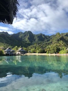 the water is crystal blue and clear with houses in the mountains behind it that are surrounded by palm trees