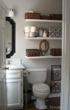 a white toilet sitting in a bathroom next to a sink and shelves with baskets on it