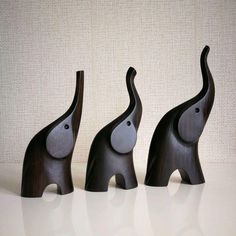 three wooden elephants standing next to each other on a white counter top in front of a beige wall