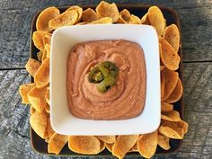 a square bowl filled with guacamole and tortilla chips on a wooden table