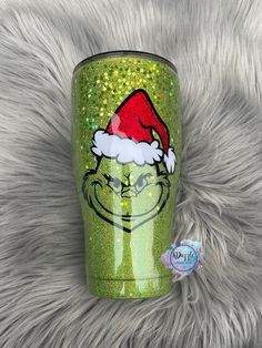 the grin face is wearing a santa hat on green glitter tumbler