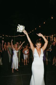 a woman in a white dress holds her arms up as she walks down the dance floor