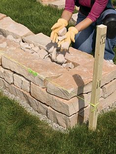 a woman is placing rocks into a brick fire pit with gloves on and gardening tools in the foreground