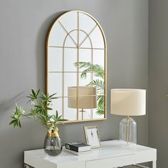 a white table topped with a mirror next to a vase filled with flowers and a lamp