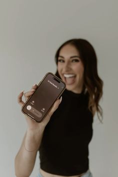 a woman holding up her cell phone in front of her face and smiling at the camera