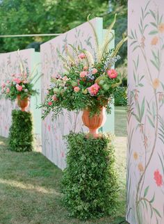 three vases filled with flowers sitting on top of green grass next to a wall