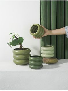 a person is holding a green vase next to some small pots and a potted plant