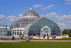 people are walking around in front of a large glass building that is surrounded by grass