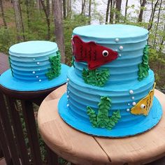 two cakes with fish on them sitting on top of a wooden table in the woods