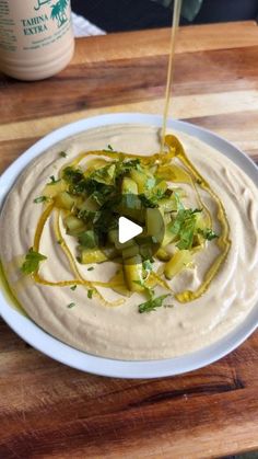 a white plate topped with hummus and green onions on top of a wooden cutting board