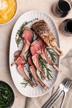 steaks with herbs on a white plate next to glasses of wine and silverware