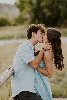 a young man and woman kissing each other in front of a field with tall grass