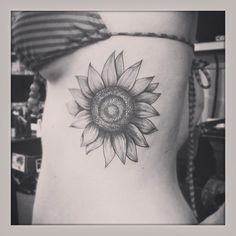 a black and white photo of a sunflower on the back of a woman's stomach