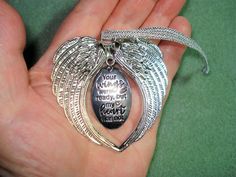 a hand holding a silver angel pendant with an engraved message on it's side