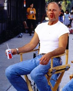 a man with blood on his face sitting in a chair holding a drink and looking at the camera