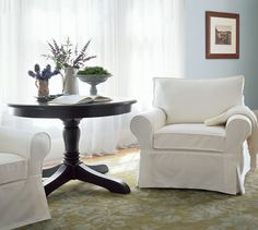 two chairs and a table in a room with white drapes on the windowsill