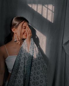 a woman standing in front of a curtain holding a scarf over her face and looking at the camera