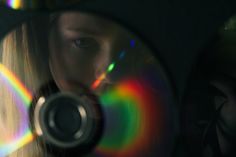 a woman looking through a magnifying glass at a rainbow colored disc in her hand