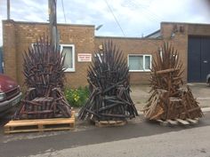 three wooden thrones sitting on pallets in front of a brick building with cars parked nearby