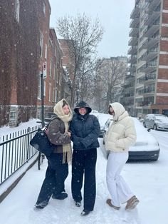 three people are standing in the snow near a fence and buildings on a snowy day