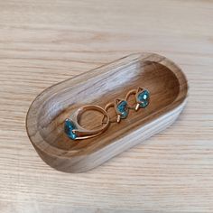 three gold rings with blue topaz sit in a wooden tray on a wood table