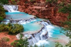 people are swimming in the blue water near waterfalls and cliffs with red rock formations