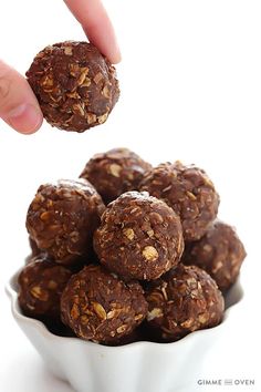 a hand is picking up some chocolate energy bites from a small white bowl filled with them